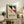 May include: Framed Bauhaus poster with geometric design featuring four colored triangles - black, blue, yellow, and red - arranged in a square pattern on cream background with German text below. Light wood frame displayed on rustic wooden sideboard alongside fern plant, ceramic vase, stacked books, and table lamp in warm-toned living room setting.