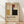 May include: Framed Bauhaus poster with geometric abstract design featuring colored rectangles in yellow, red, blue, and black on cream background. German text below describes the design school from 1919-1933. Light wood frame leaning against white wall on wooden floor with soft natural lighting and fabric shadows.