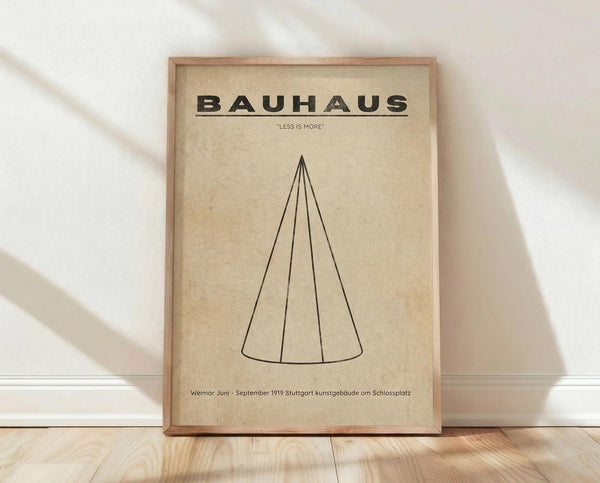 May include: Framed Bauhaus poster print with beige aged paper background featuring black geometric cone design and "LESS IS MORE" text, displayed in thin wood frame leaning against white textured wall on light wooden floor with natural window lighting creating soft shadows