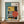 May include: Framed geometric abstract poster in Bauhaus style featuring teal, yellow, orange, black and cream colored shapes including circles, rectangles and linear elements. Text reads "BAUHAUS" vertically and "FORM FOLLOWS FUNCTION" at bottom with "01" in corner. Displayed on wooden sideboard next to white ceramic vase and stacked books against cream wall with white trim.