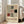May include: Framed Bauhaus-style poster with geometric grid pattern in black, red, and gray rectangles and squares on cream background, displayed in white frame leaning against wall next to beige sofa in bright modern living room with large windows and hardwood floors.