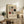 May include: Framed Bauhaus-inspired geometric art print with cream background featuring black, red, and olive green rectangles and squares in grid formation, displayed on rustic wooden sideboard alongside books, ceramic vase, and fern plant in modern living room setting with leather chair and neutral decor.