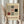 May include: Person in cream-colored clothing holding framed Bauhaus-style poster featuring geometric shapes in black, red, and gray on beige background. Dried pampas grass visible to left. Light wooden frame against neutral interior setting with soft natural lighting and beige curtains.