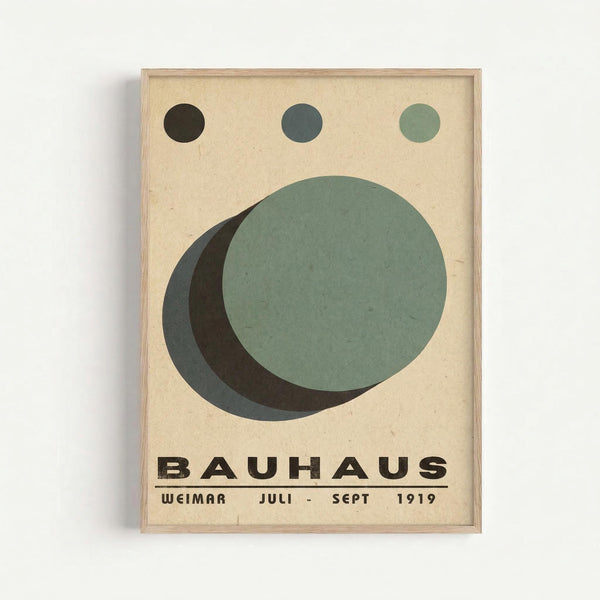 Minimalist poster featuring geometric circles in black, dark gray, and sage green arranged on cream background. Three small circles aligned at top with larger overlapping circles below creating layered effect. Bold black text reads "BAUHAUS" with "WEIMAR JULI - SEPT 1919" underneath. Natural wood frame against white wall. Clean modernist design with muted earth tones and simple typography reflecting Bauhaus aesthetic principles.