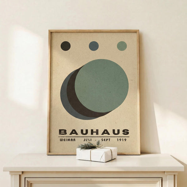 May include: Framed Bauhaus-style poster with geometric design featuring overlapping circles in sage green, dark green, and charcoal gray on cream textured background, displayed on light wood console table against white wall with small wrapped gift box beside it