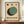 May include: Framed Bauhaus-style poster with geometric design featuring overlapping green and dark circles on cream background, three small circles above, displayed on wooden sideboard with white ceramic vase and books in neutral-toned room with white paneled walls.