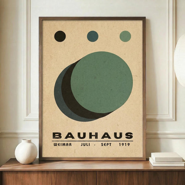 May include: Framed Bauhaus-style poster with geometric design featuring overlapping green and dark circles on cream background, three small circles above, displayed on wooden sideboard with white ceramic vase and books in neutral-toned room with white paneled walls.