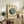 May include: Framed Bauhaus-style poster with geometric circles in sage green, dark green, and black on cream background, displayed on rustic wooden sideboard alongside books, ceramic vase, and potted fern in modern living room setting with leather armchair and warm neutral tones.