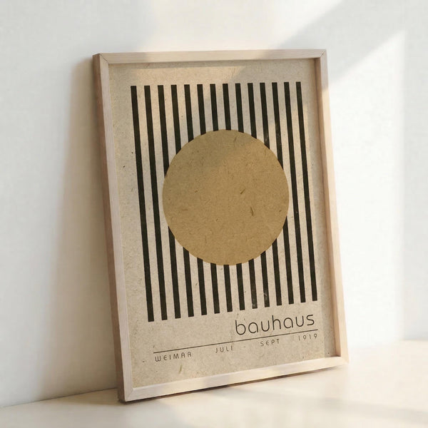 May include: Framed Bauhaus-style poster with vertical black stripes and tan circle, displayed against white wall. Cream textured background with "bauhaus," "weimar," and "juli sept 1919" text at bottom. Natural wood frame, minimalist geometric design in neutral earth tones.