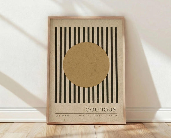 May include: Framed Bauhaus-style poster with black vertical stripes and tan circle on beige textured background, displayed in light wood frame against white wall on wooden floor with soft natural lighting and fabric shadows