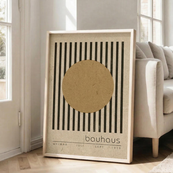 May include: Framed Bauhaus-style poster with beige textured background featuring black vertical lines and tan circle, displayed on wooden floor next to beige sofa in bright room with white walls and large windows