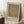 May include: Framed Bauhaus-style poster with beige textured background, black vertical lines, and tan circle design element. Light wood frame leaning against white wall corner next to white coffee cup on wooden block and beige knit throw blanket on fluffy white rug.