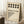 May include: Framed Bauhaus poster with cream background featuring black circles arranged in two rows and geometric dot pattern forming corner design. Bold black text reads "BAUHAUS" with "FORM FOLLOWS FUNCTION" subtitle and German exhibition details. Displayed leaning against white wall corner on textured white rug, with coffee cup on wooden block nearby and cozy blanket visible.