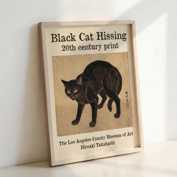 May include: Framed poster print featuring a black cat in an arched, hissing pose with yellow eyes on aged beige background. The artwork shows Japanese-style illustration with visible artist signature and red stamp. White matted frame with museum attribution text below the image, leaning against white wall on light surface.
