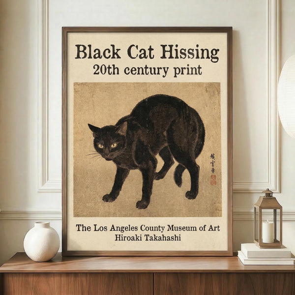 May include: Framed vintage-style poster featuring a black cat in defensive posture with arched back and alert expression, rendered in traditional Japanese art style on aged beige paper background. The wooden-framed artwork is displayed on a mid-century modern wooden sideboard alongside a white ceramic vase and brass lantern, against cream wainscoting walls.