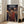 May include: Framed anime poster leaning against white wall next to beige sofa in bright living room. Artwork shows dark-haired samurai character in red kimono holding sword on traditional Japanese street at dusk with lanterns and crowds. Japanese and English text at top. Natural wood frame on hardwood floor with sunlight streaming through windows.