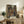 May include: Framed anime poster displaying a bustling Japanese street scene with colorful characters in traditional clothing, lanterns hanging overhead, and detailed architecture. The artwork features warm earth tones and traditional Japanese text at the bottom. Shown in a light wood frame on a rustic wooden sideboard alongside decorative pottery, books, and a fern plant in a cozy living room setting.