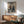 May include: Framed anime poster showing two samurai warriors dueling with swords amid stylized ocean waves, displayed above a wooden credenza in a modern living room with mid-century chair, white lamp, and soft natural lighting casting shadows on white walls.