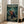 May include: Framed anime-style poster displayed in bright living room with beige furniture. Shows three samurai characters in traditional Japanese clothing wielding swords in bamboo forest setting. Green and teal color scheme with dramatic lighting. Medium-sized wooden frame leaning against white wall near cream-colored sofa. Japanese text visible at top along with English subtitle about swords, sunflowers, and samurai themes.