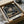 May include: Anime poster featuring a dark-haired samurai character with sword in traditional Japanese indoor setting, displayed in black frame inside cardboard packaging with protective wrapping, surrounded by brown paper and packaging materials on white surface