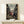 May include: Framed anime poster displayed on light wood shelf against white wall. Shows three samurai characters with swords in traditional Japanese street setting. Japanese and English text at top reads "Samurai Champloo" and "Destiny Lies on the Hip." Characters wear red, pink, and blue clothing in detailed illustration style. Small white wrapped gift box sits in front of poster. Natural wood frame matches shelf. Soft lighting creates gentle shadows on wall.