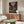 May include: Framed anime poster displayed above wooden sideboard in modern living room setting. Poster shows samurai characters in action scene on traditional Japanese street at sunset with Japanese text. Room features white curved chair, glass-top coffee table, white table lamp, and neutral decor with natural lighting.