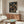 May include: Framed anime poster showing samurai character in red jacket walking through traditional Japanese street with paper lanterns at night. Poster displayed above wooden mid-century modern credenza in minimalist living room with white curved chair, oval glass coffee table, and white walls.