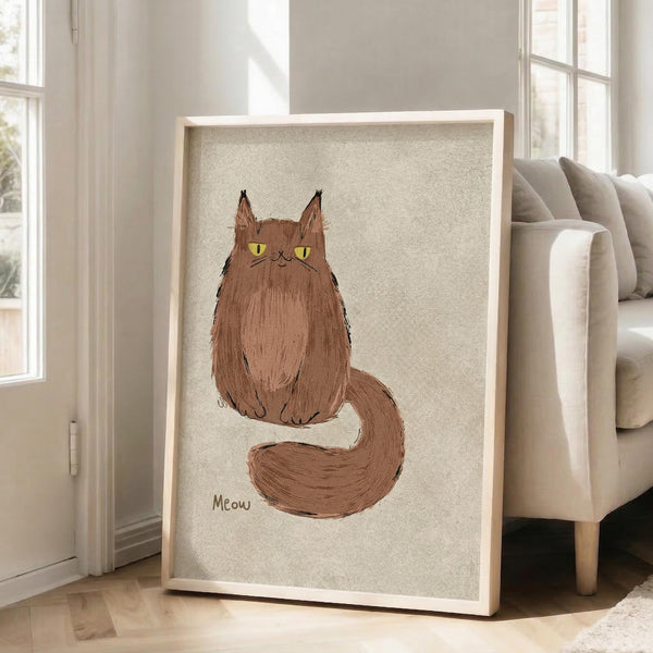May include: Framed artwork leaning against white wall beside beige armchair in bright room with large windows. The poster features a fluffy brown cat with yellow eyes and long tail sitting upright on textured beige background, with "Meow" text below. Light wood frame, approximately 2-3 feet tall, creates warm contrast against neutral interior decor.