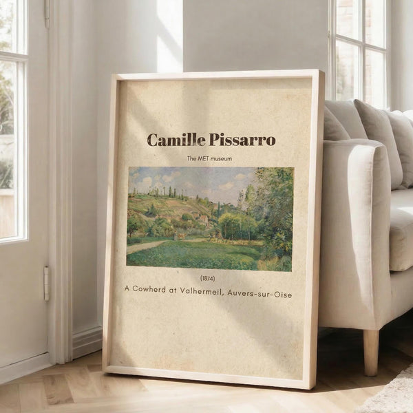May include: Framed art print leaning against white wall next to beige sofa in bright room with windows. Print features Impressionist landscape painting with green meadows, rolling hills, and cloudy sky in soft pastels. Cream-colored poster with brown text displays artist name, museum attribution, artwork title and date in clean typography within light wood frame.