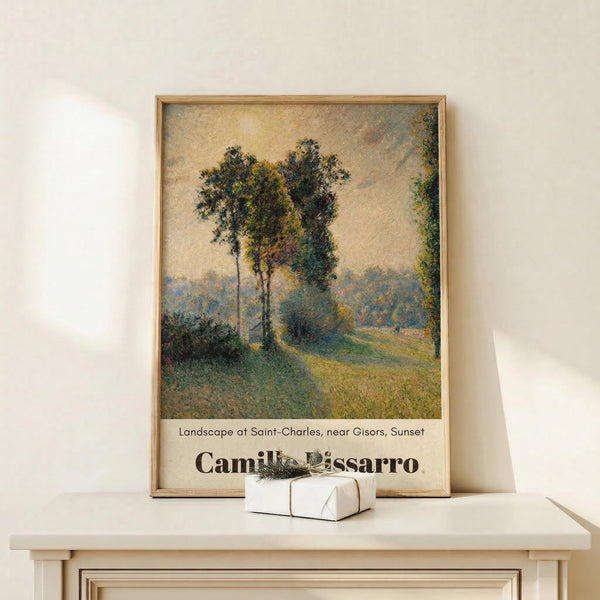 May include: Framed poster print of an impressionist landscape painting showing tall trees along a winding country path at sunset, displayed on a light wood surface against a cream wall. The artwork features soft brushstrokes in golden yellows, greens, and muted earth tones. A small white gift box with twine sits in front of the natural wood frame.