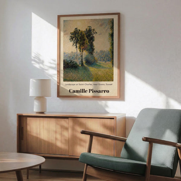 May include: Framed poster of an impressionist landscape painting showing tall trees beside a winding path at sunset, with golden and green tones throughout the pastoral scene. The artwork is displayed above a wooden sideboard with sliding doors, next to a white ceramic table lamp and mid-century modern green upholstered armchair with wooden frame. Natural sunlight creates geometric shadows across the white wall and wooden furniture in this contemporary living room setting.