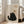 May include: Large framed poster leaning against white wall next to beige sofa in bright living room. The artwork shows a black textured cat with golden eyes sitting upright, looking up at a hanging ball of yarn. The cat appears painted in rough, fuzzy brushstrokes with "Meow" text below. The frame is light wood against cream-colored paper background. Natural sunlight streams through tall windows.