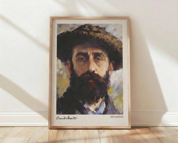 May include: Framed art print of a bearded man in a wide-brimmed hat, painted in impressionist style with loose brushstrokes in earth tones of brown, green, and purple. The portrait shows expressive eyes and full dark beard against a muted background. Text below reads "Claude Monet" and "self portrait." Natural wood frame with white matting, leaning against white textured wall on light wooden floor with soft natural lighting.