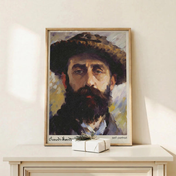 May include: Framed self-portrait painting of bearded man wearing wide-brimmed hat, displayed on light wooden shelf against cream wall. Impressionist style artwork shows expressive brushstrokes in earth tones and blues. Small wrapped gift box with greenery sits beside the thin wooden frame. Soft natural lighting creates gentle shadows on minimalist styled surface.