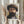 May include: Person holding framed art print of bearded man wearing wide-brimmed hat, painted in impressionist style with warm earth tones and expressive brushstrokes. Light wood frame with white matting, held against neutral background near window with dried wheat stems visible to left.