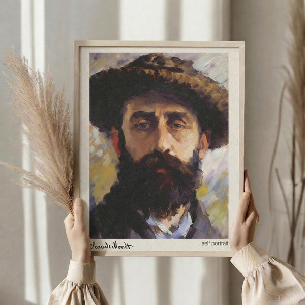 May include: Person holding framed art print of bearded man wearing wide-brimmed hat, painted in impressionist style with warm earth tones and expressive brushstrokes. Light wood frame with white matting, held against neutral background near window with dried wheat stems visible to left.
