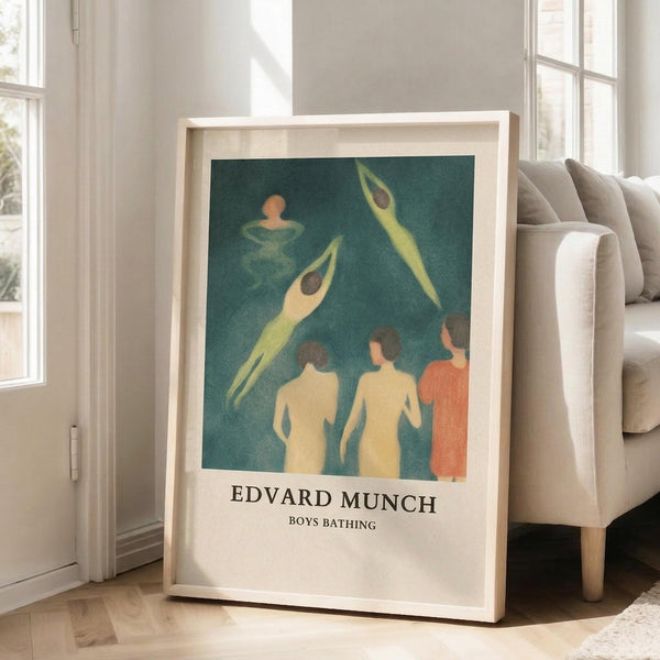 May include: Framed art print leaning against white wall next to beige sofa in bright room with large windows. Print shows Edvard Munch's expressionist painting of nude figures swimming and diving in teal-green water, with yellow and orange skin tones. Text below reads "EDVARD MUNCH BOYS BATHING" on cream background. Light wood frame, soft natural lighting creates shadows on wooden floor.