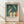 May include: Framed art print leaning against white wall on light wood floor with natural window light casting shadows. The poster features Edvard Munch's expressionist painting showing figures bathing in teal-green water - pale yellow nude forms and one figure in orange, with elongated swimmers above. Light wood frame with cream matting surrounds the artwork in this minimalist room setting.