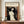 May include: Framed art print of Munch's Madonna showing a woman with flowing dark hair and pale skin against swirling orange and black background, with small skeletal figure in corner. Print displayed on wooden credenza beside white ceramic vase and books in elegant room with cream walls and white trim molding.