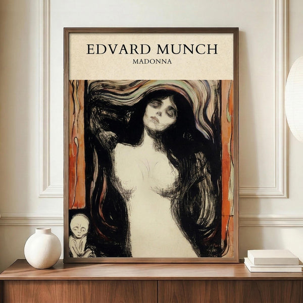 May include: Framed art print of Munch's Madonna showing a woman with flowing dark hair and pale skin against swirling orange and black background, with small skeletal figure in corner. Print displayed on wooden credenza beside white ceramic vase and books in elegant room with cream walls and white trim molding.