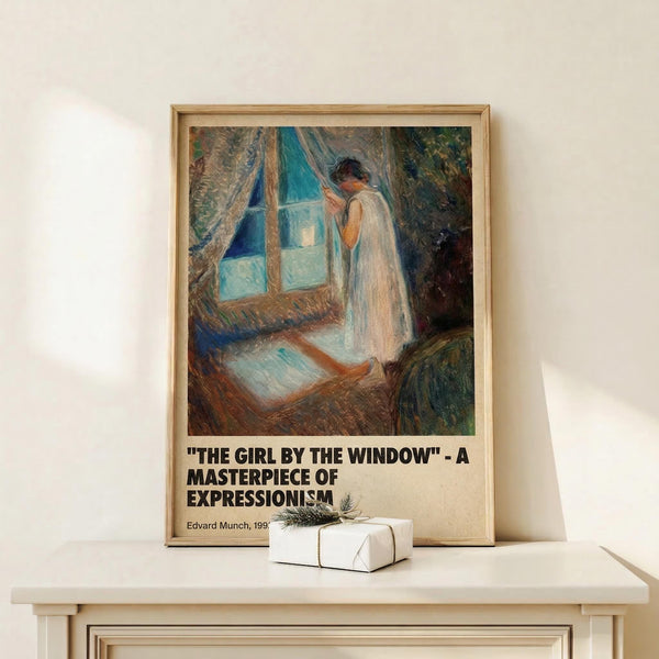 May include: Framed art print showing a woman in white dress standing by a window with blue curtains in an impressionistic style. The poster features text identifying it as "The Girl by the Window" by Edvard Munch from 1893, described as a masterpiece of Expressionism. The wooden-framed print leans against a white wall on a light wooden shelf, with a small wrapped gift box beside it.