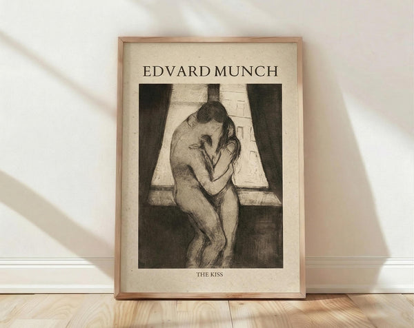 May include: Framed art print of Edvard Munch's "The Kiss" displayed on wooden floor against white wall with natural lighting. Print shows two nude figures embracing in black and white etching style, matted in cream with "EDVARD MUNCH" and "THE KISS" text, housed in natural wood frame.