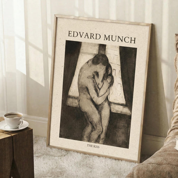 May include: Framed reproduction of Munch's "The Kiss" etching showing two embracing figures in black and white sketch style, leaning against white wall corner next to wooden block table with coffee cup and saucer, beige textured rug visible below