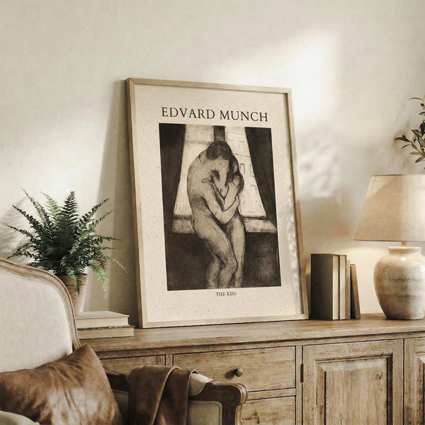 May include: Framed beige and black art print of two embracing figures displayed on rustic wooden sideboard next to fern plant, books, and ceramic vase in neutral-toned living room setting with cream chair and throw blanket