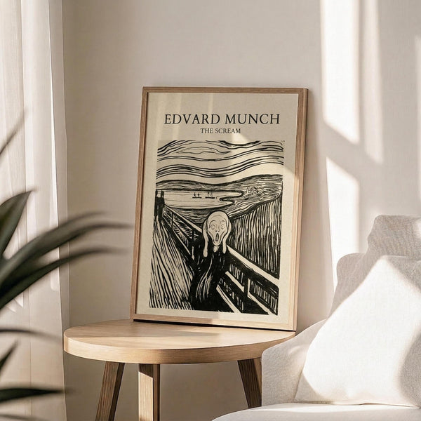 May include: Framed poster featuring Edvard Munch's iconic The Scream artwork in black ink on cream paper, displayed on a round wooden side table next to a beige upholstered chair. Natural sunlight streams across white walls, with green plant leaves visible in the corner. The print shows the famous expressionist figure with hands to face on a bridge with swirling sky lines above.