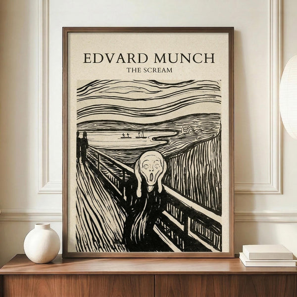May include: Framed black and white reproduction of Munch's famous expressionist artwork showing a figure with hands to face in an anguished scream, standing on a bridge with swirling sky lines. The print has cream background with dark linear details, displayed in thin brown frame on wooden sideboard alongside white ceramic vase and stacked books in neutral-toned room with white walls and crown molding.