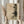 May include: Person in cream sweater holding framed artwork featuring abstract geometric lines overlaid with dark pine tree branches on aged beige paper background. Natural light streams through white curtains while dried wheat stalks are held in other hand, creating warm minimalist home decor scene with earthy tones.