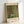 May include: Framed art print leaning against white wall showing Gustav Klimt's colorful garden painting with vibrant sunflowers, red poppies, and wildflowers in green foliage. Light wood frame with cream matting displays museum-style poster with artist name at bottom. Soft natural lighting creates gentle shadows on clean white surface.
