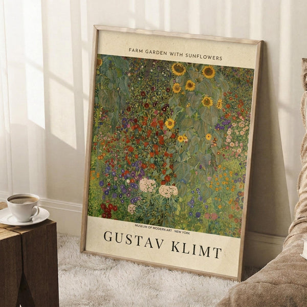May include: A framed museum-style poster reproduction of Gustav Klimt's colorful garden painting featuring vibrant sunflowers, wildflowers, and lush green foliage in his distinctive decorative style. The cream-colored poster with black text is displayed in a light wooden frame, leaning against white walls on a textured white rug beside a cozy armchair and wooden side table with coffee cup.