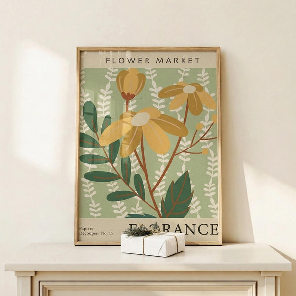 May include: Vintage-style botanical poster in light wood frame featuring yellow daisy-like flowers and green foliage against sage green background with "FLOWER MARKET" and "FRANCE" text, displayed on white wooden surface next to small wrapped gift with twine and dried botanicals against cream wall